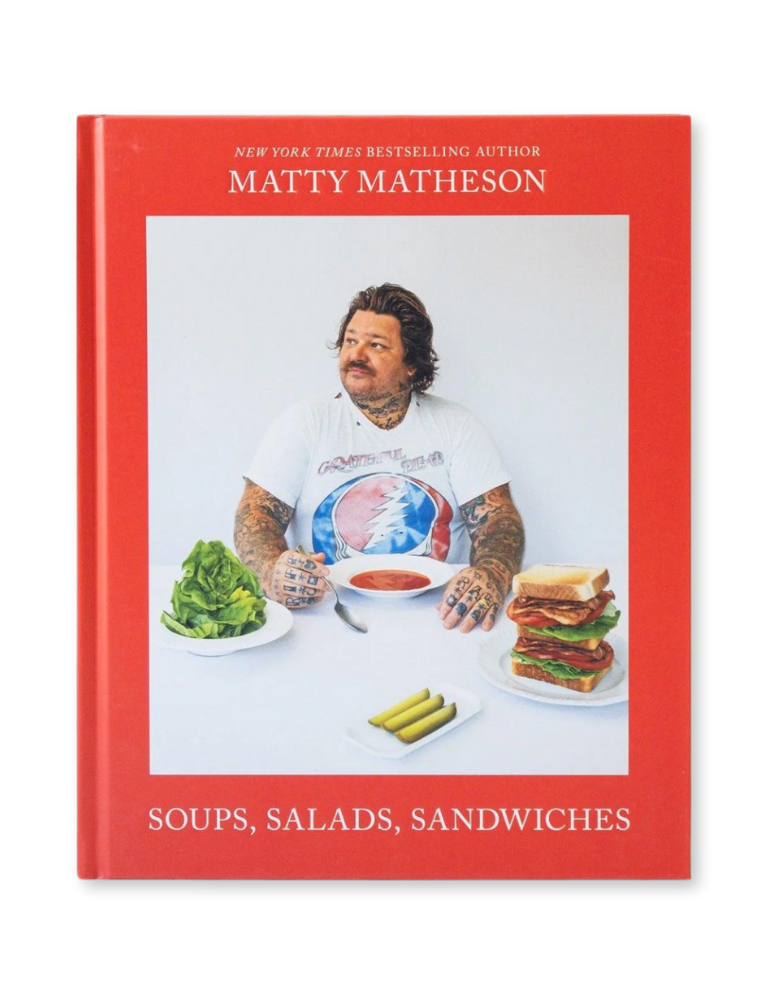A cover image of the book titled 'Matty Matheson: Soups, Salads, Sandwiches' featuring the author, Matty Matheson, with a red background. He is seated at a table with food in front of him, including a salad and sandwiches.