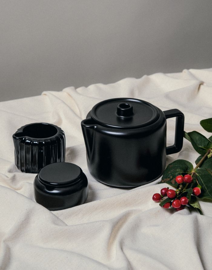 Black Matheson ceramic pourover and cups on a white fabric background with greenery.